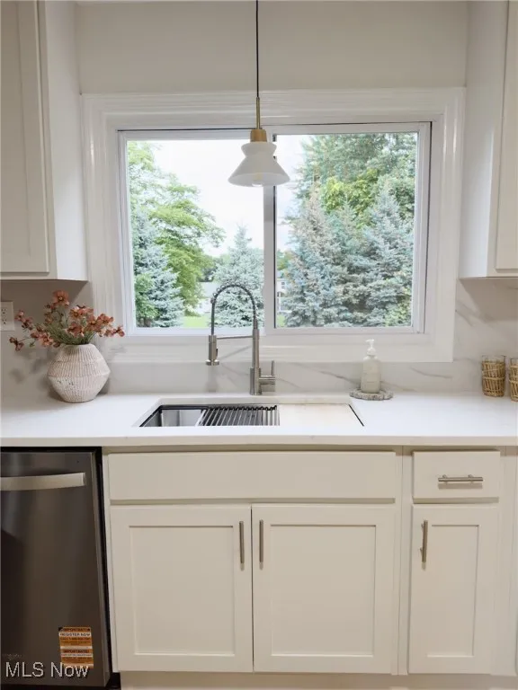 Kitchen featuring white cabinets, stainless steel dishwasher, pendant lighting, and light stone counters