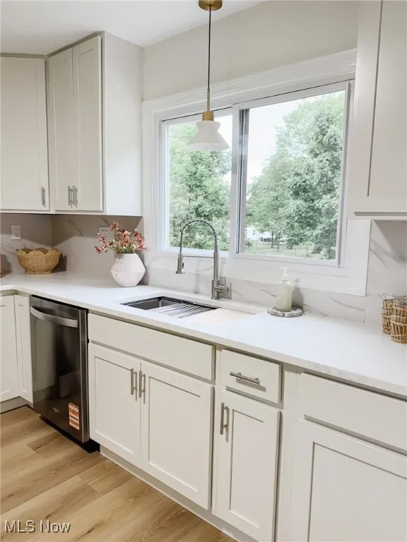 Kitchen featuring light wood-style floors, stainless steel dishwasher, white cabinetry, hanging light fixtures, and light stone countertops