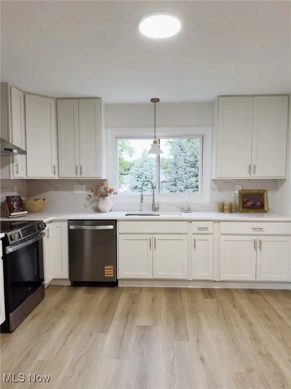 Kitchen with pendant lighting, appliances with stainless steel finishes, white cabinets, and light wood finished floors