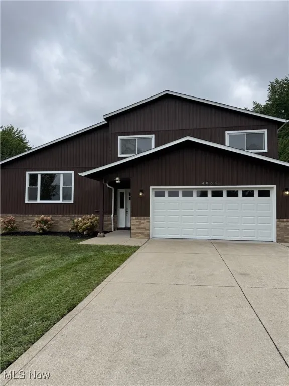View of front facade with driveway, brick siding, a front yard, and an attached garage
