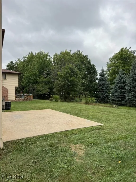 View of green lawn featuring a patio and view of wooded area