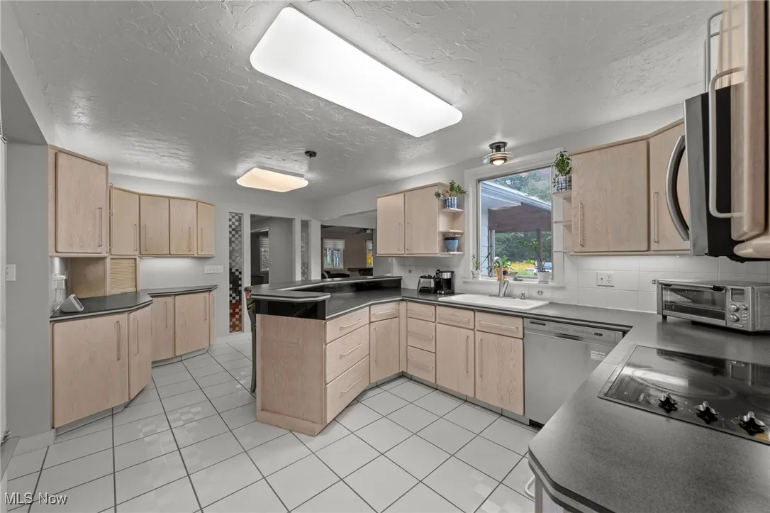 Kitchen with light brown cabinets, light tile patterned floors, stainless steel appliances, a peninsula, and dark countertops