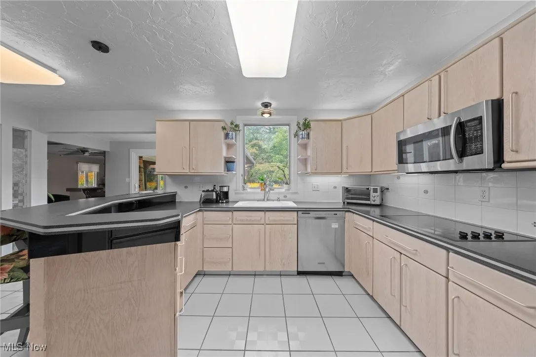 Kitchen featuring light brown cabinets, a peninsula, dark countertops, a ceiling fan, and a textured ceiling