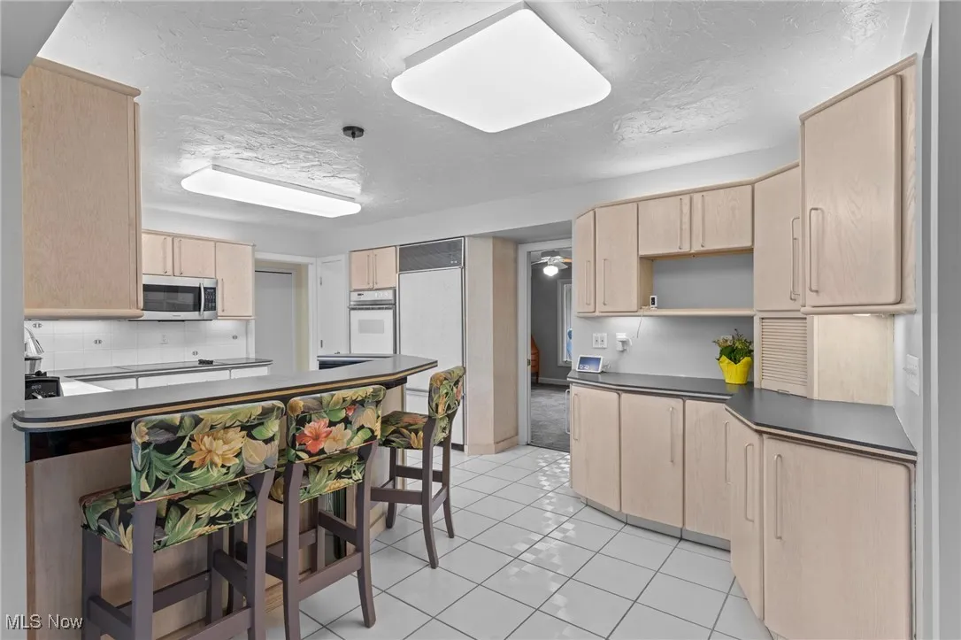 Kitchen with light brown cabinets, light tile patterned floors, a textured ceiling, paneled built in refrigerator, and dark countertops