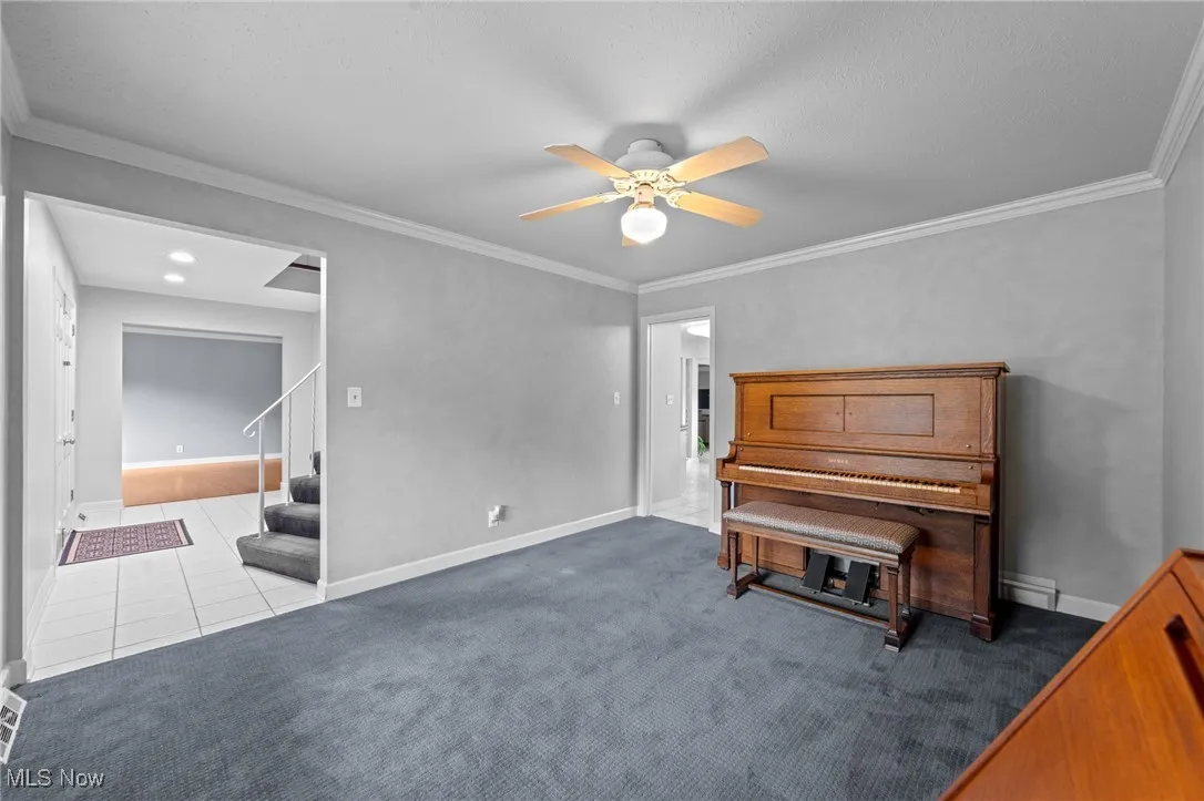 Living area with ornamental molding, ceiling fan, carpet, tile patterned flooring, and stairs