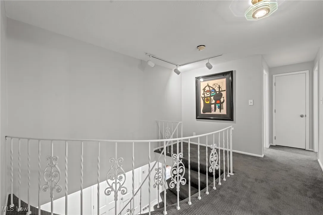 Corridor with an upstairs landing, track lighting, and dark colored carpet