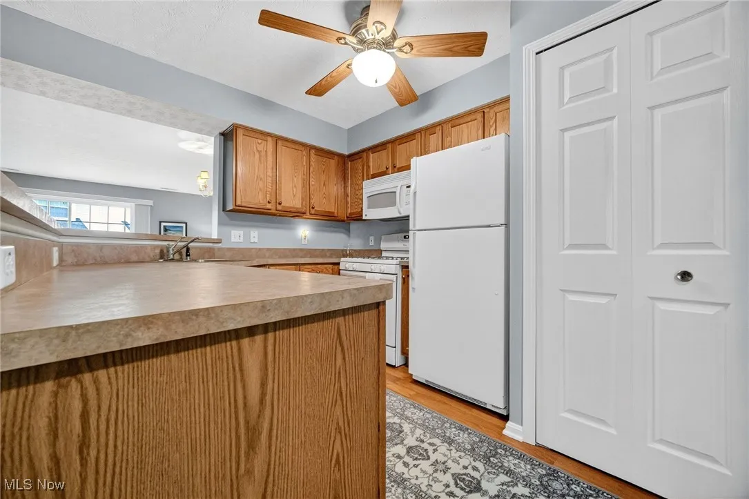 Kitchen with white appliances, brown cabinets, light wood-style floors, light countertops, and a ceiling fan