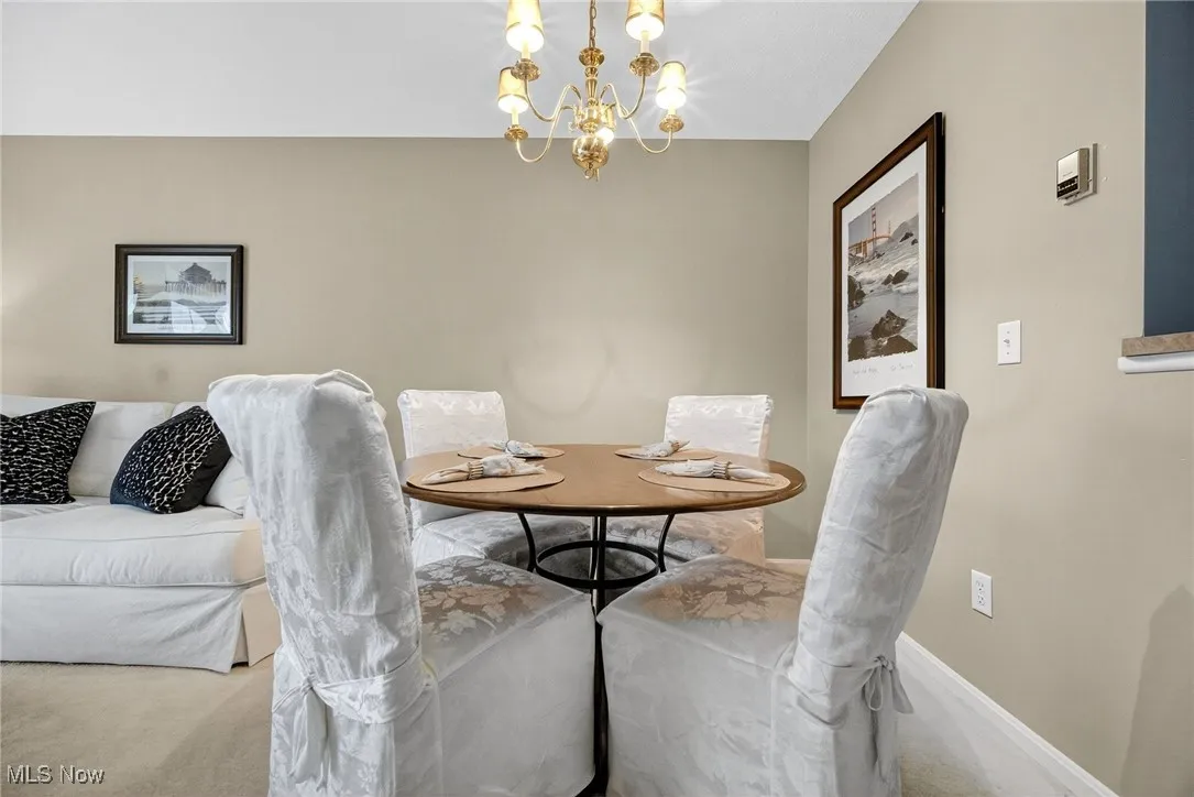 Carpeted dining space with a chandelier and baseboards