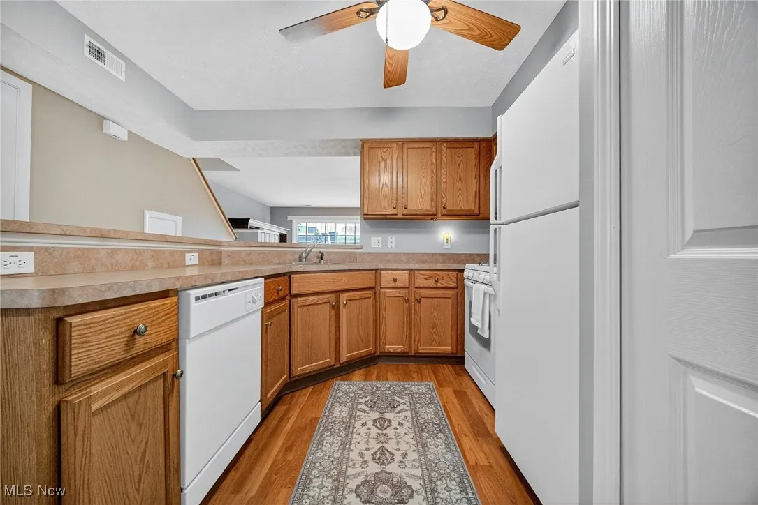 Kitchen featuring brown cabinetry, white appliances, light wood-type flooring, light countertops, and a peninsula