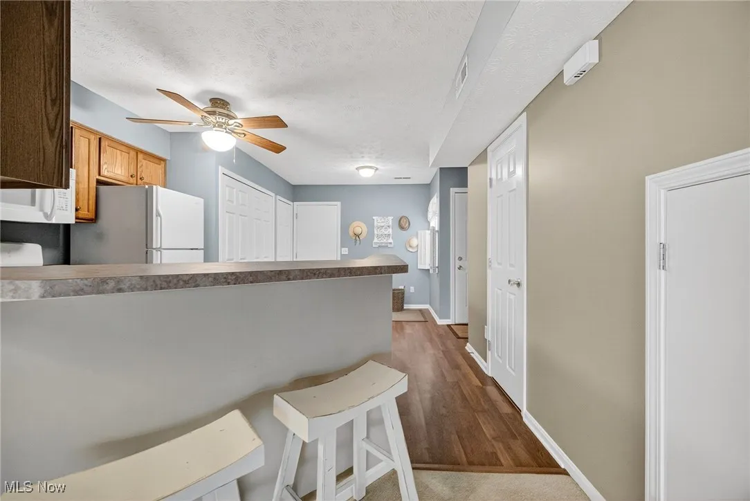 Kitchen featuring a breakfast bar, a textured ceiling, white appliances, dark wood-style flooring, and a ceiling fan
