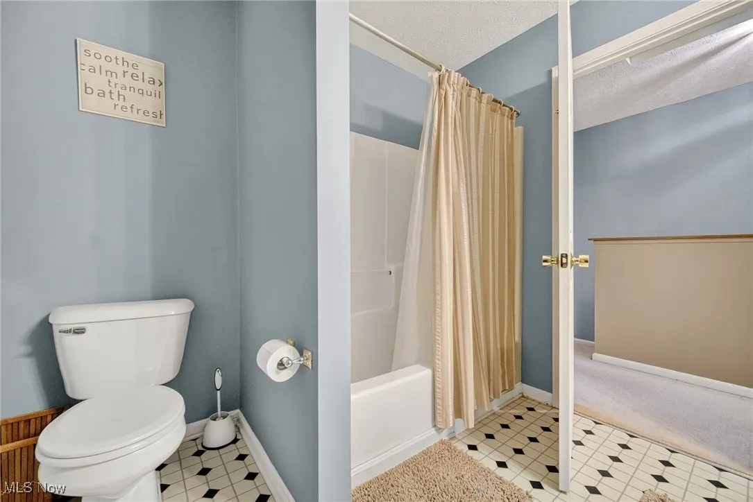 Bathroom with shower / bath combination with curtain, tile patterned floors, and a textured ceiling