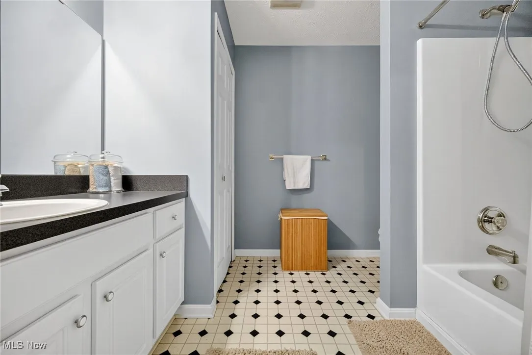Bathroom featuring bathtub / shower combination, vanity, a textured ceiling, and light tile patterned floors