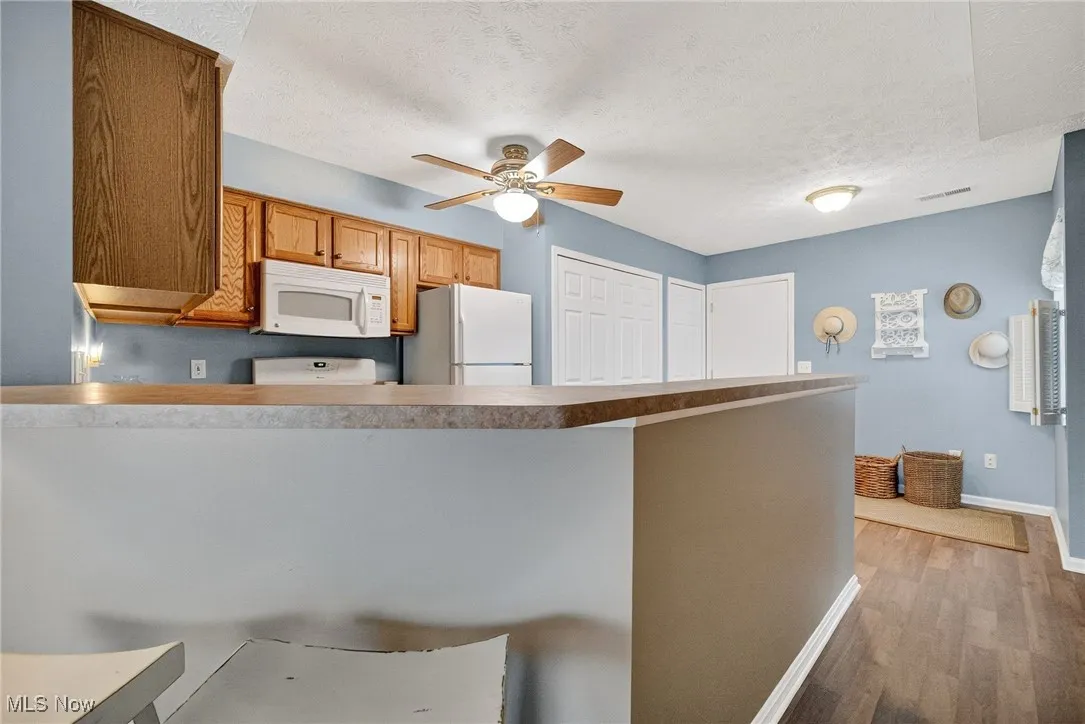 Kitchen with white appliances, brown cabinets, light wood finished floors, a ceiling fan, and a textured ceiling
