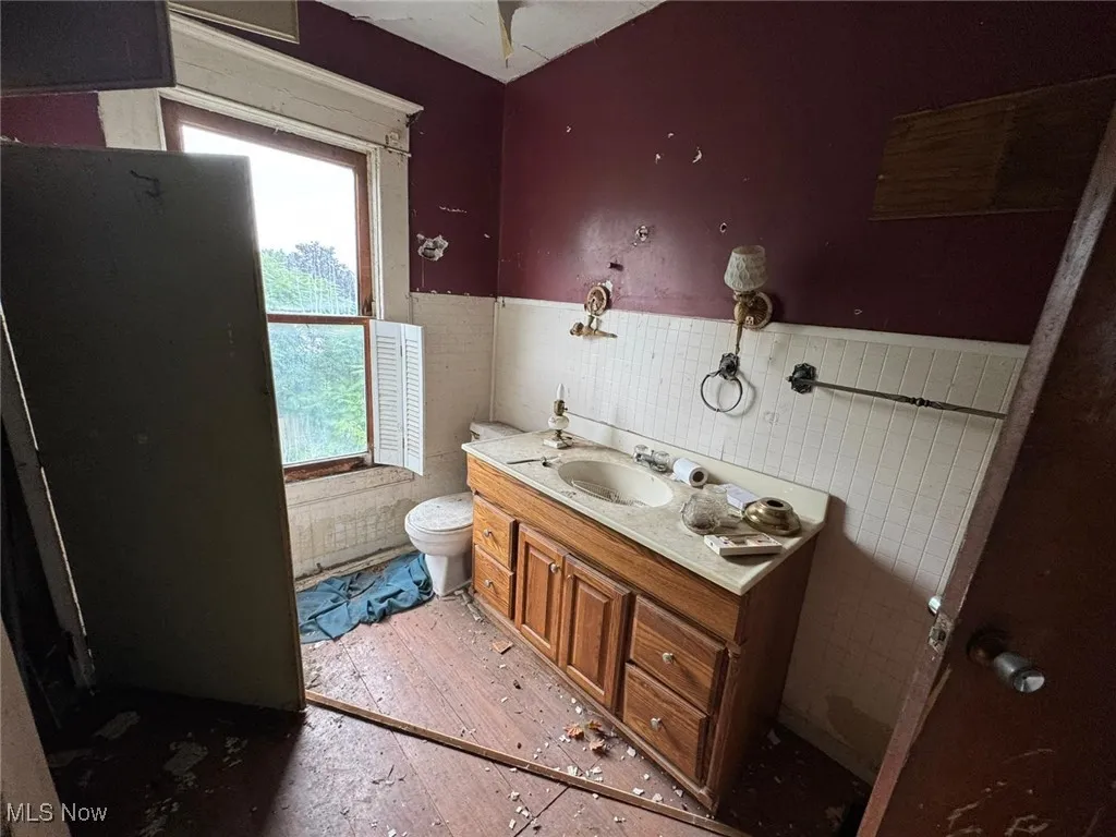 Half bathroom with tile walls, vanity, a wainscoted wall, and light wood-style flooring