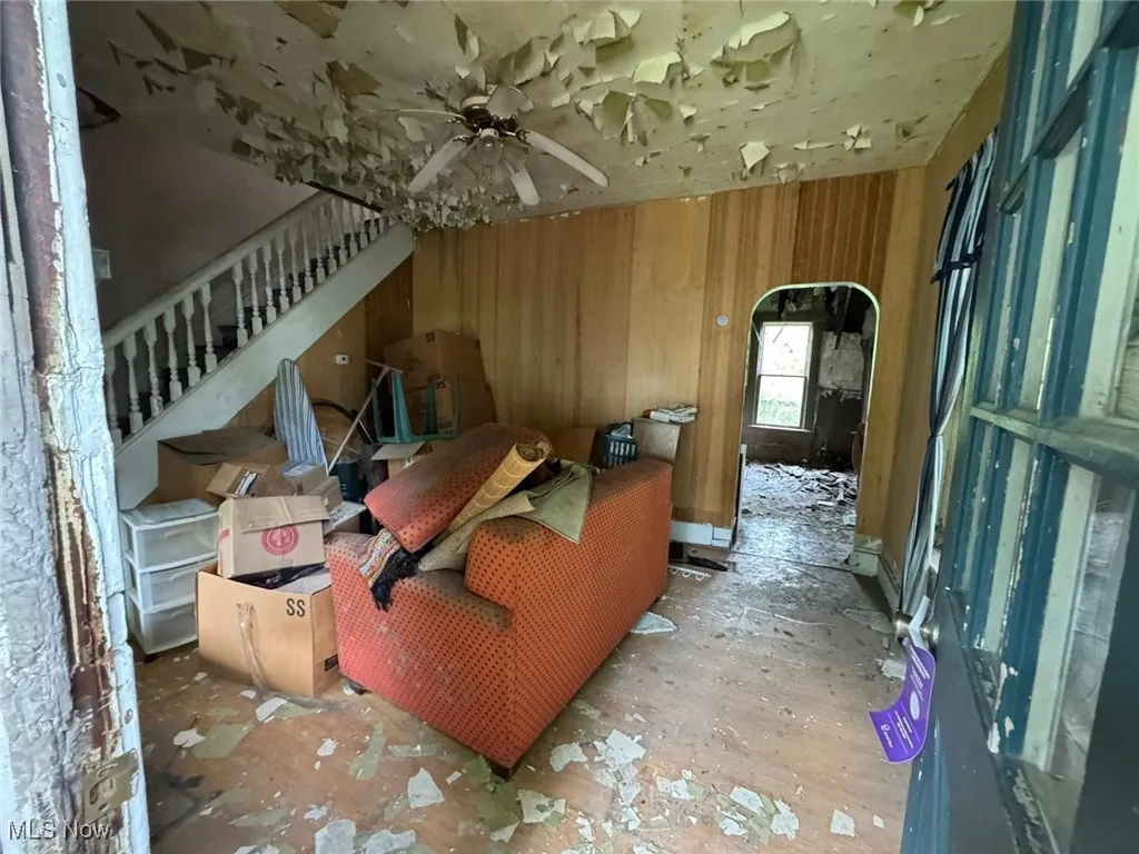 Living room with wood walls, arched walkways, stairway, and a ceiling fan