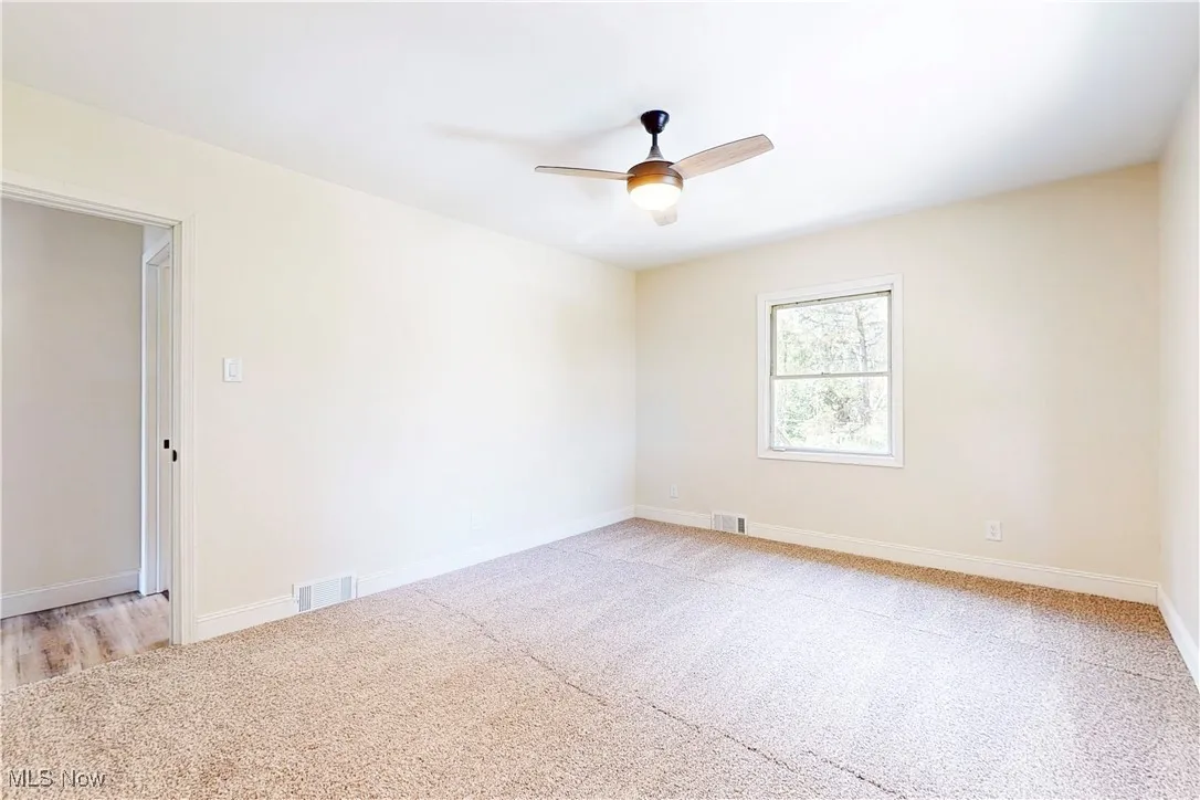 Empty room with light colored carpet and ceiling fan