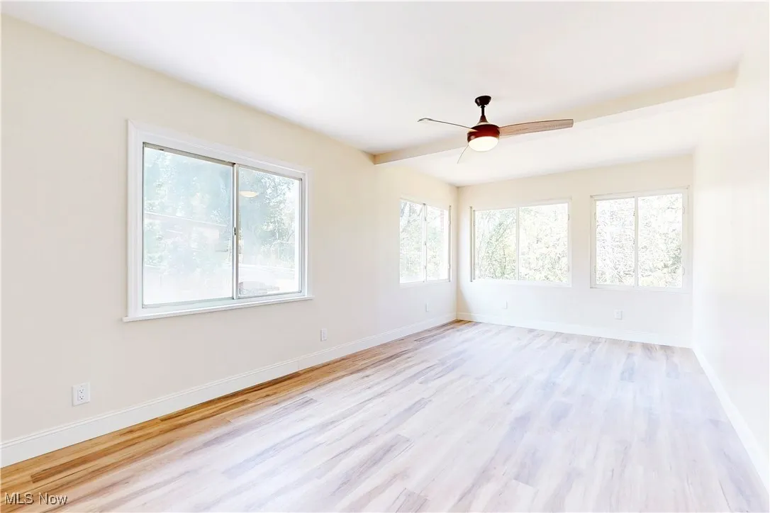 Unfurnished room with light wood-style flooring, a ceiling fan, and beam ceiling