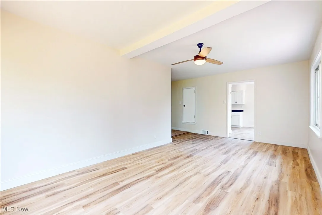 Spare room featuring beam ceiling, light wood-style floors, and ceiling fan