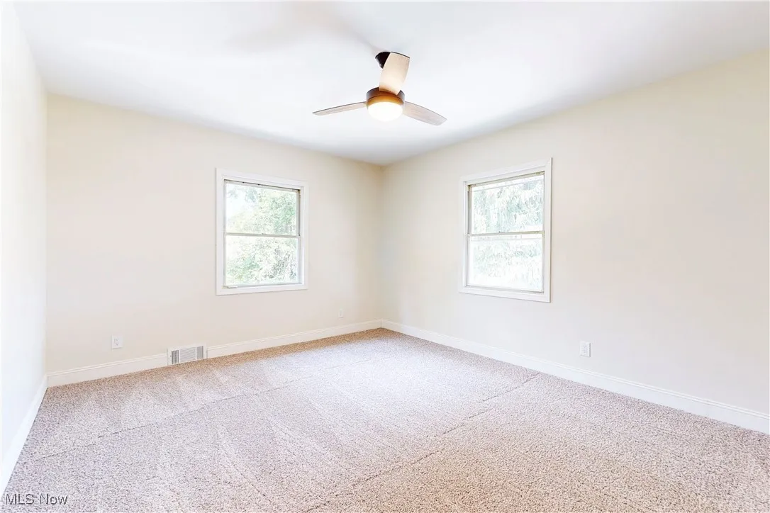 Empty room with light carpet and a ceiling fan