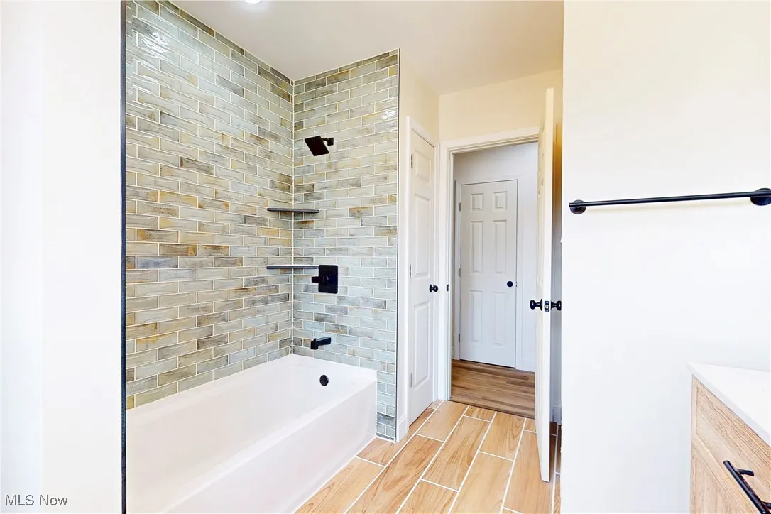 Full bathroom with washtub / shower combination, wood tiled floors, and vanity