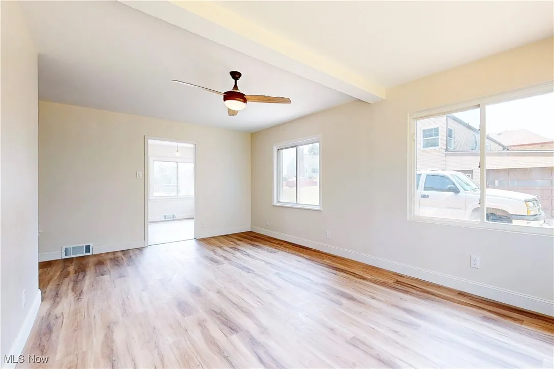 Empty room with healthy amount of natural light, light wood-style flooring, a ceiling fan, and beamed ceiling