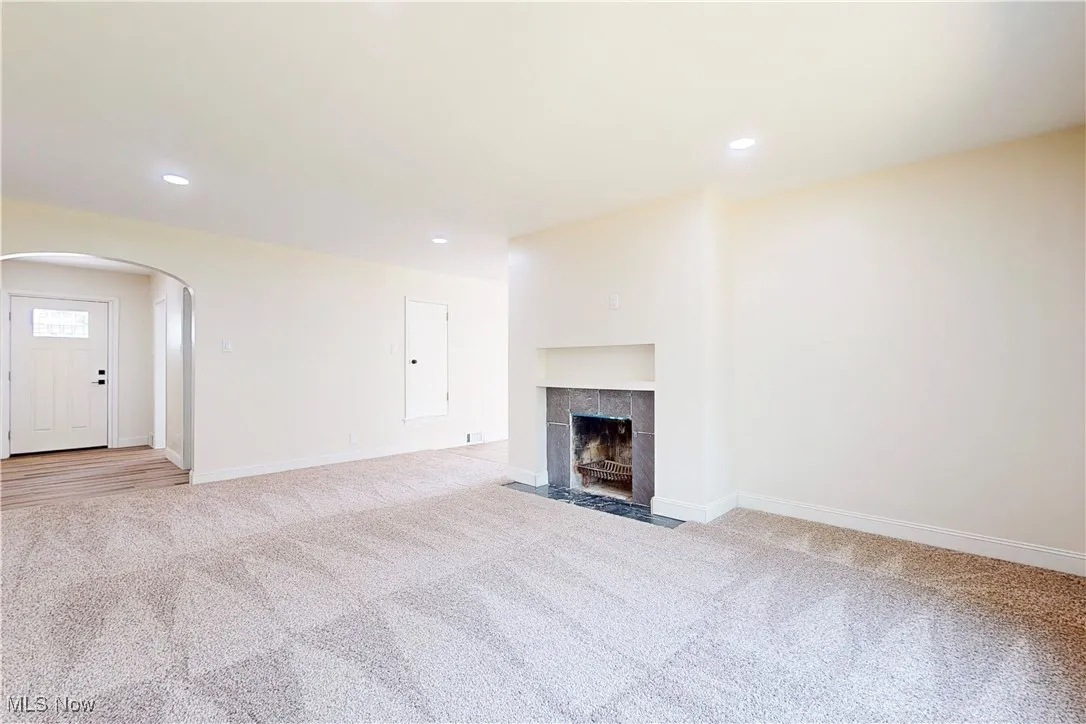 Unfurnished living room with arched walkways, light carpet, recessed lighting, and a fireplace