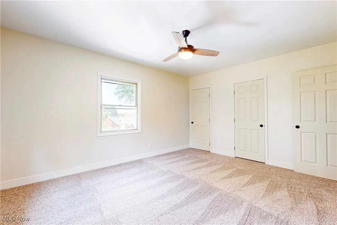Unfurnished bedroom with two closets, light colored carpet, and a ceiling fan