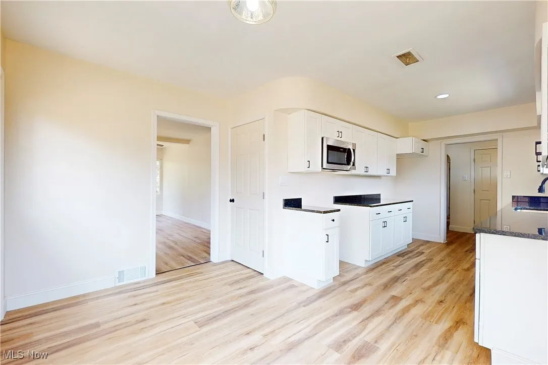 Kitchen featuring white cabinetry, light wood-style flooring, stainless steel microwave, dark stone countertops, and recessed lighting