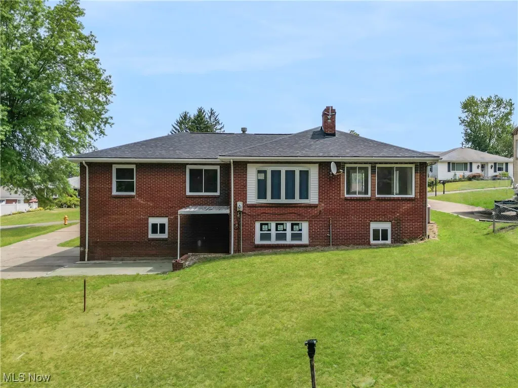 Back of house with brick siding, a lawn, a chimney, and a shingled roof