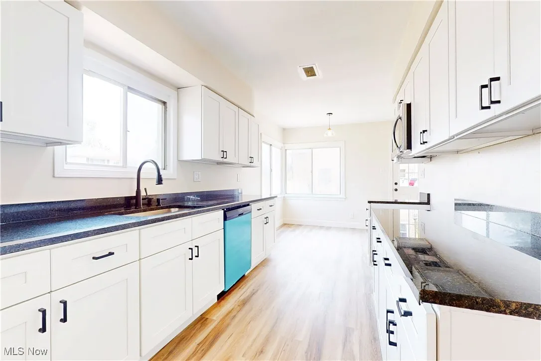 Kitchen with white cabinets, light wood finished floors, dishwasher, decorative light fixtures, and stainless steel microwave