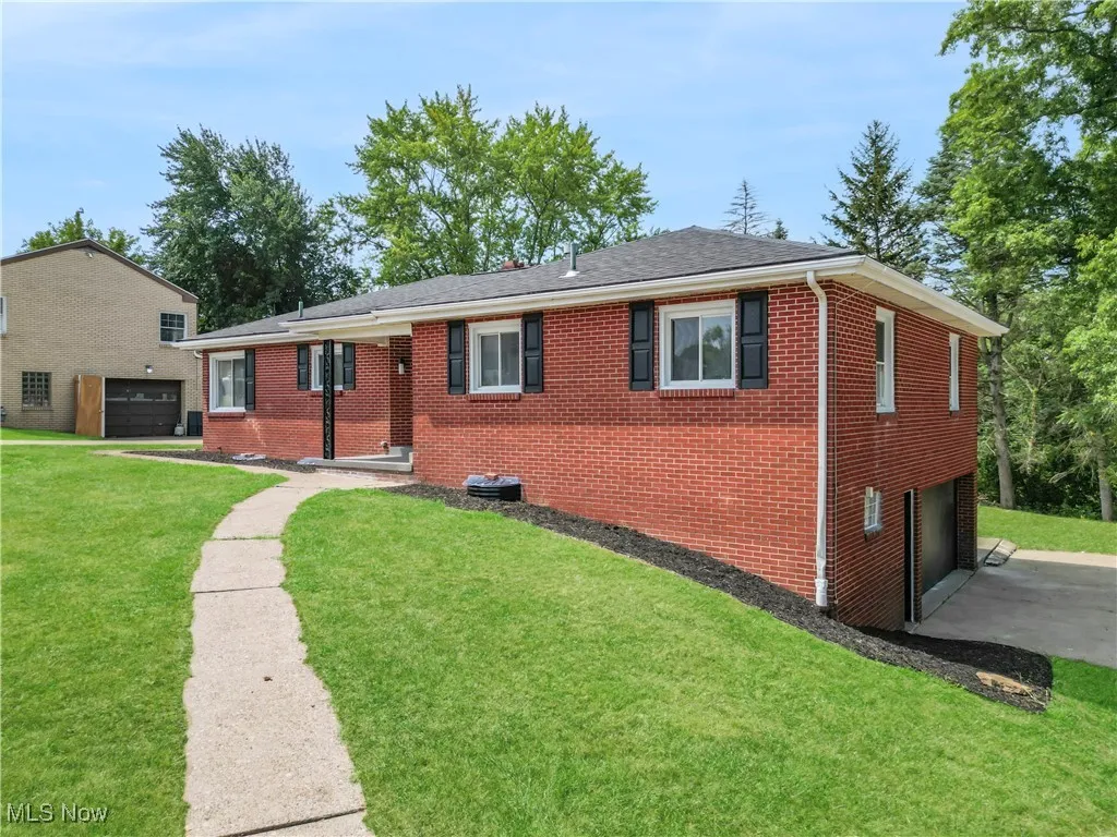 Single story home with an attached garage, brick siding, a front lawn, driveway, and a shingled roof