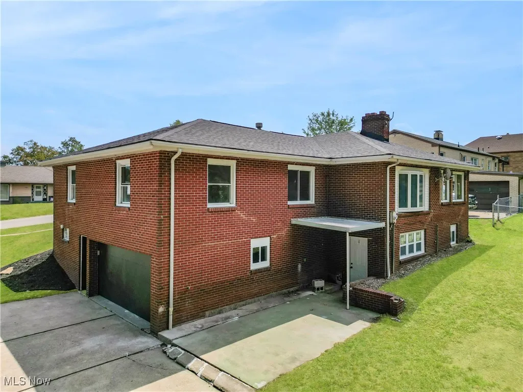 Back of property with a yard, brick siding, a chimney, and roof with shingles