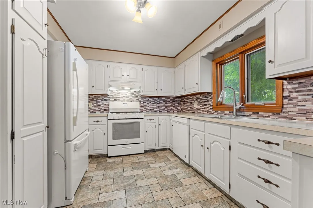 Kitchen featuring white cabinetry, white appliances, light countertops, tasteful backsplash, and ornamental molding