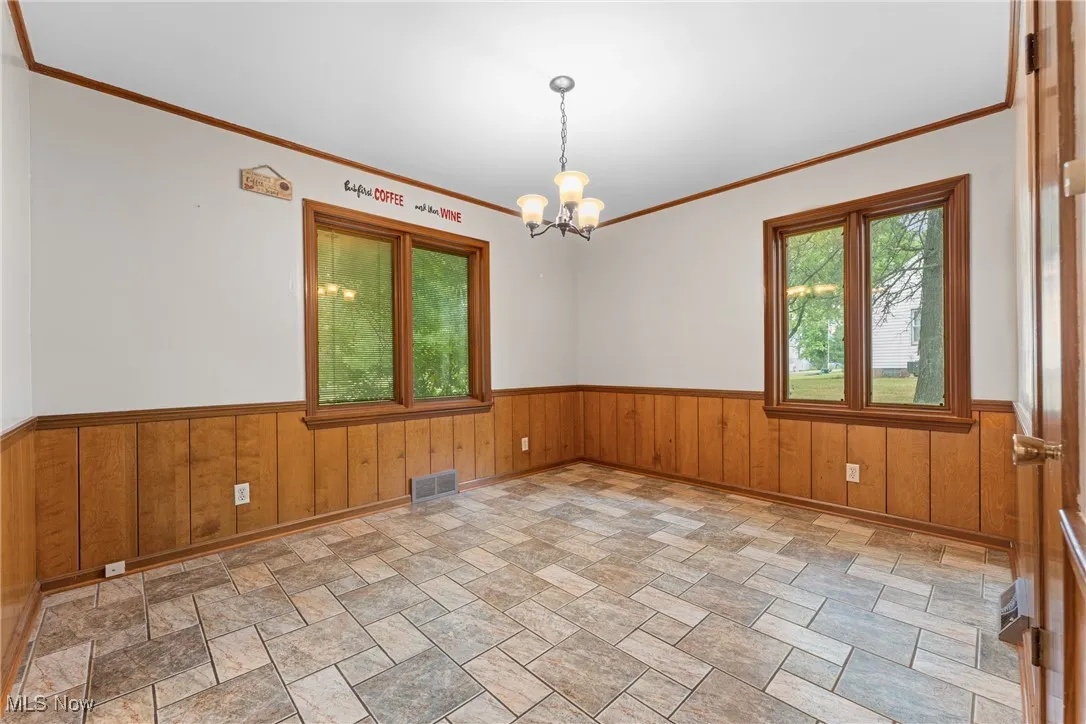Spare room featuring a wainscoted wall, wooden walls, crown molding, and a chandelier