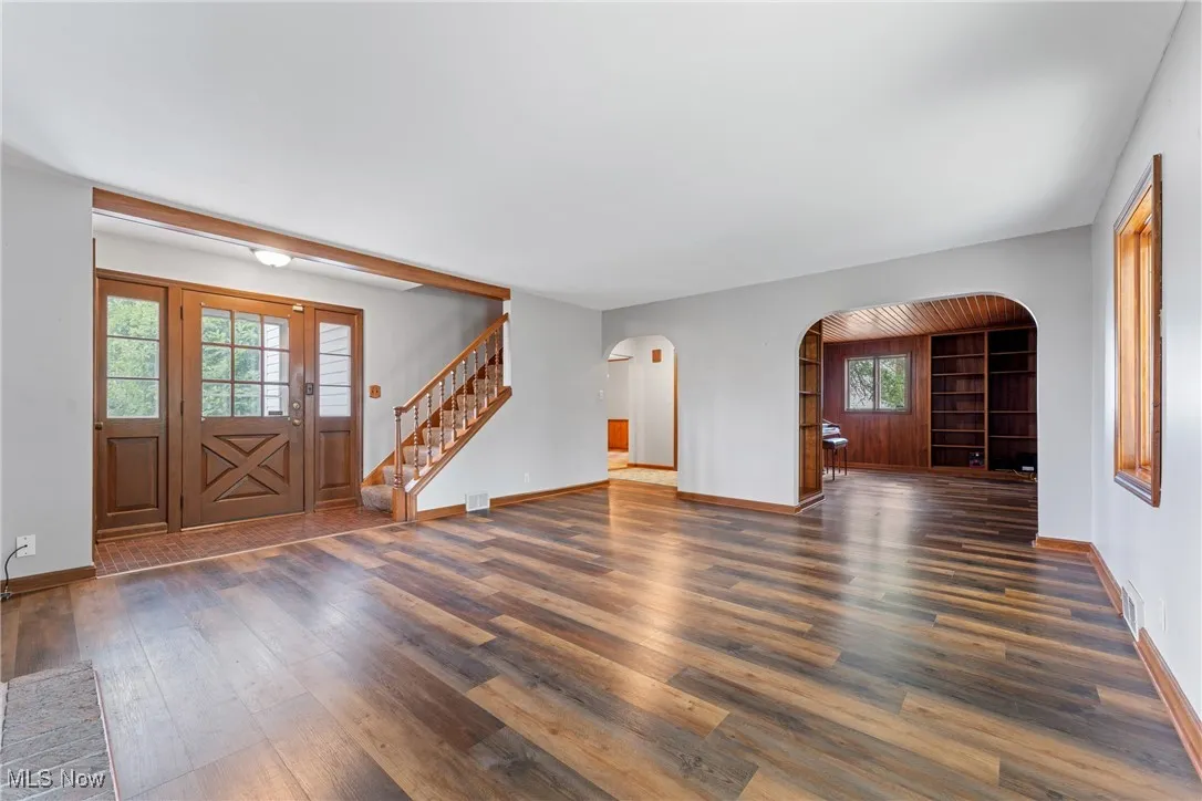 Unfurnished living room with dark wood-style floors, arched walkways, and stairway