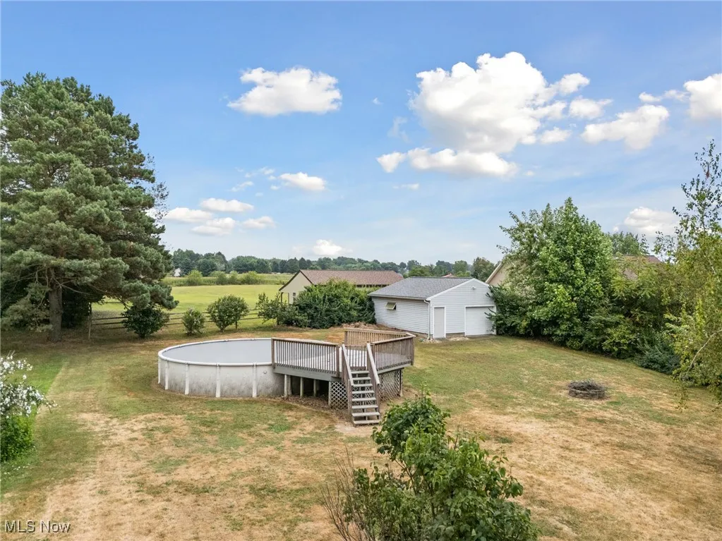 View of green lawn featuring a deck, a garage, an outdoor structure, stairs, and view of scattered trees