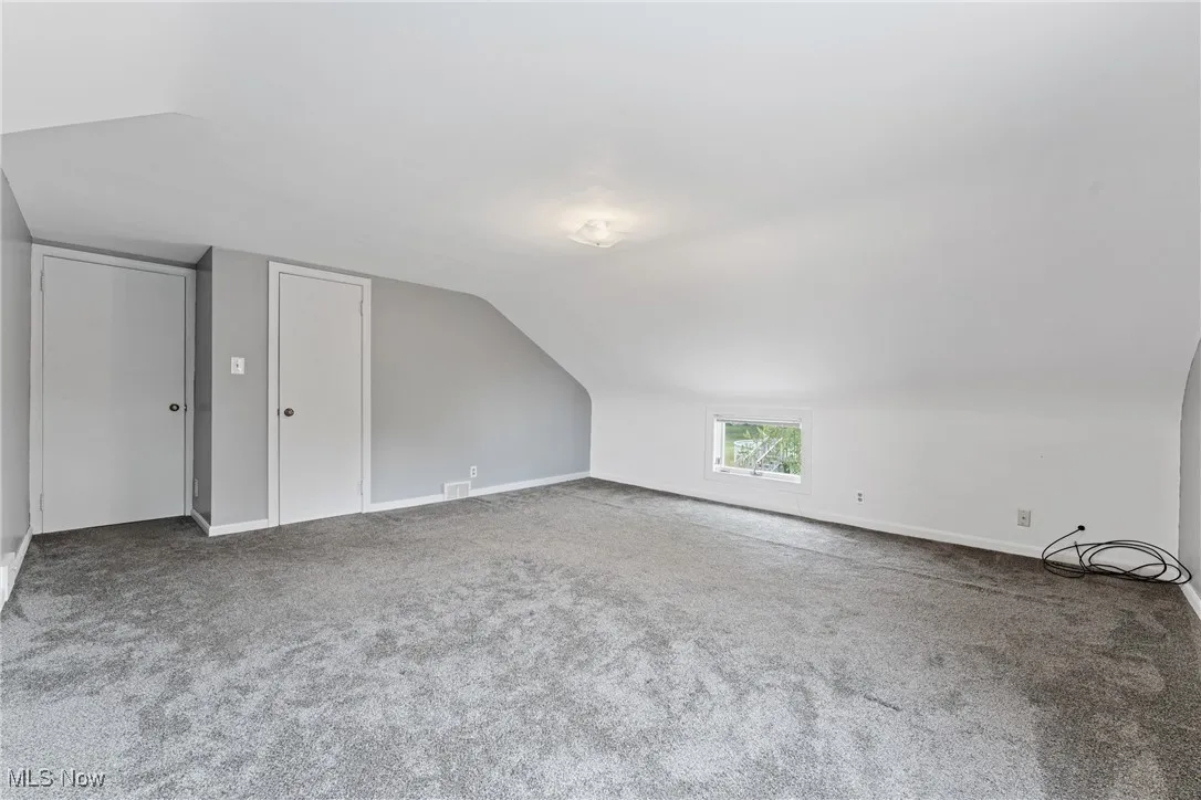 another view of the primary bedroom with lofted ceiling and carpet flooring