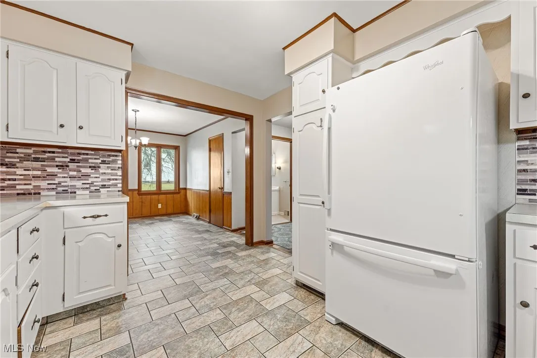 Kitchen featuring tasteful backsplash, light countertops, freestanding refrigerator, and crown molding