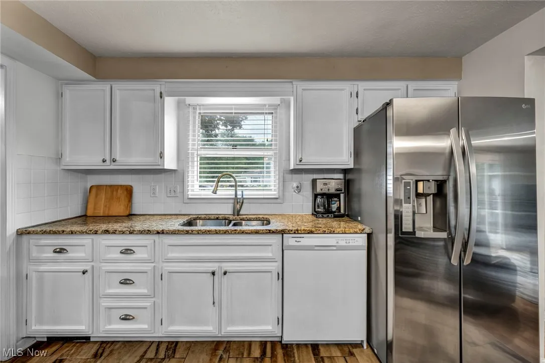 Kitchen featuring stainless steel fridge, white dishwasher, white cabinetry, decorative backsplash, and a textured ceiling