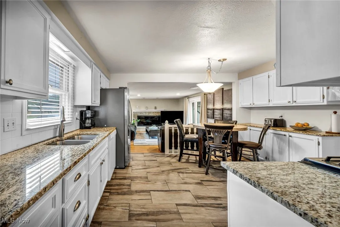 Kitchen featuring white cabinets, decorative light fixtures, wood tiled floors, light stone countertops, and freestanding refrigerator