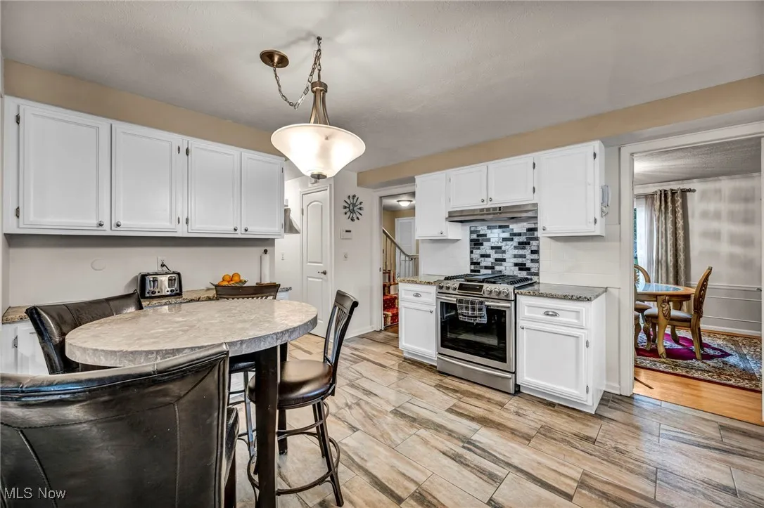 Kitchen with white cabinetry, gas range, tasteful backsplash, hanging light fixtures, and light wood-style flooring