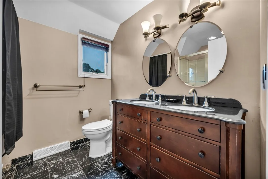 Bathroom featuring double vanity, a shower with door, and dark marble finish flooring