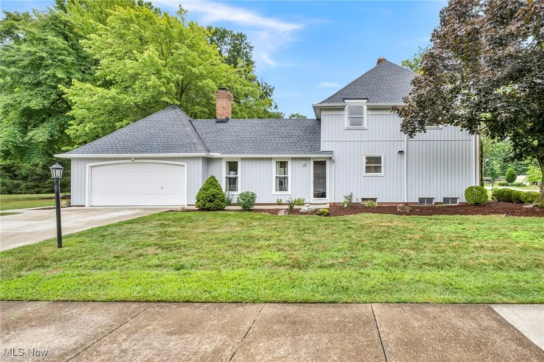 Traditional-style home featuring a shingled roof, a garage, concrete driveway, a chimney, and a front lawn