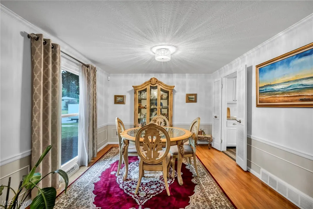 Dining space featuring light wood-style flooring, wainscoting, a decorative wall, a textured ceiling, and crown molding