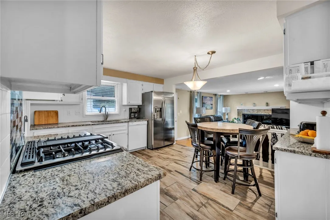 Kitchen with white cabinets, light stone countertops, open floor plan, decorative light fixtures, and stainless steel appliances