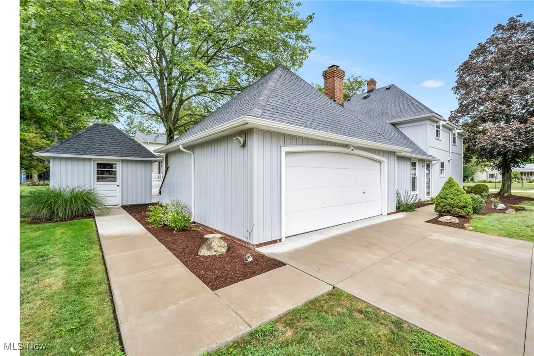 View of property exterior featuring a garage, a shingled roof, a chimney, driveway, and a lawn