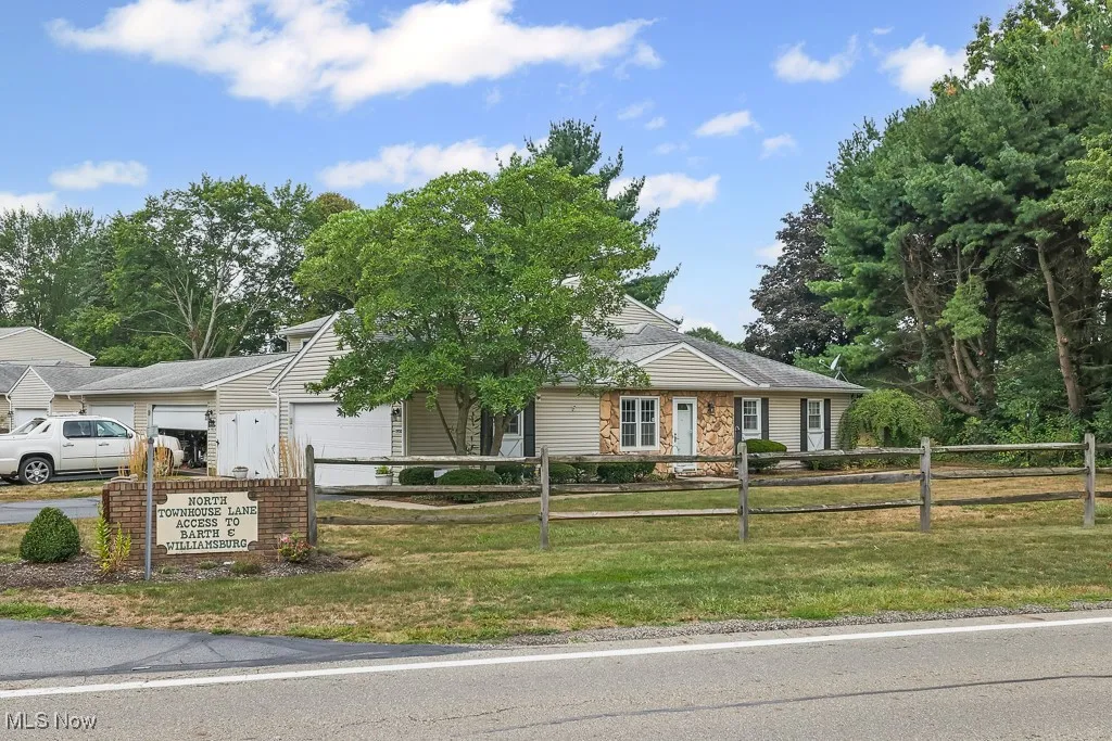 Ranch-style home with a garage, stone siding, a fenced front yard, and driveway