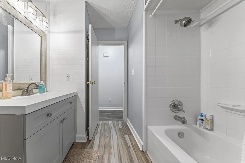 Bathroom with bathing tub / shower combination, vanity, light wood finished floors, and a textured ceiling