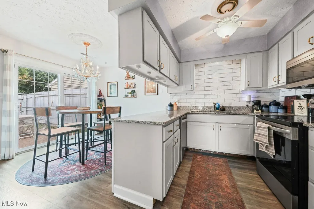 Kitchen with appliances with stainless steel finishes, tasteful backsplash, a textured ceiling, light stone countertops, and a peninsula
