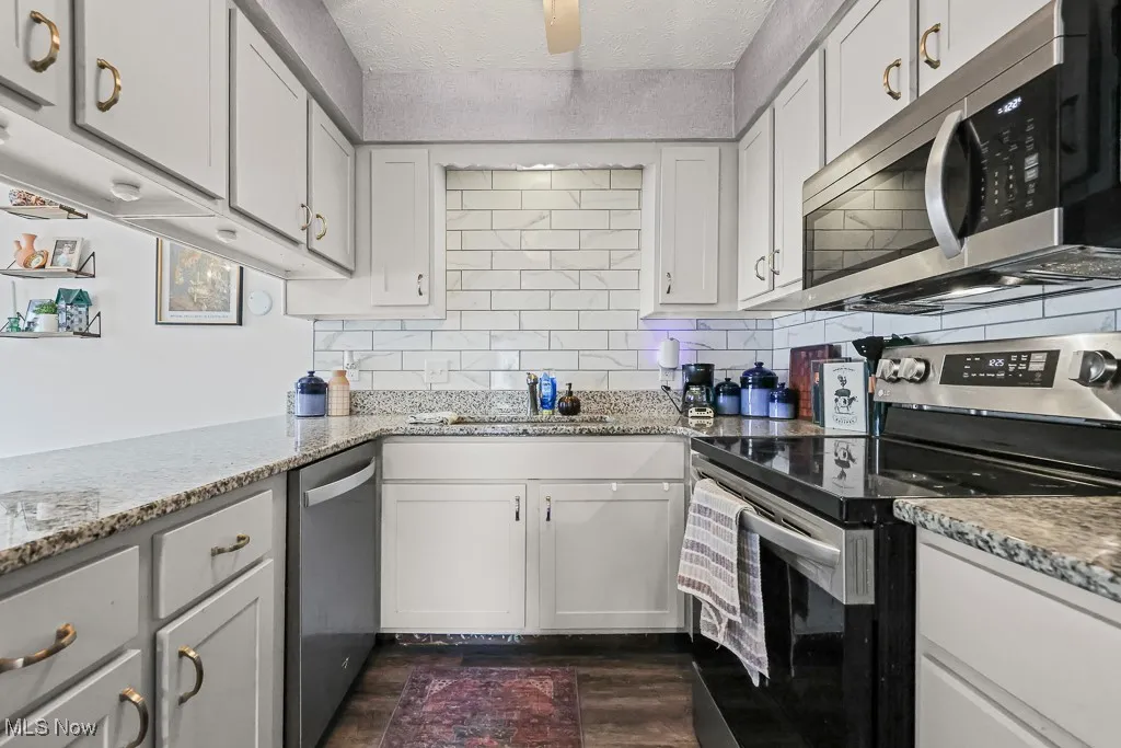 Kitchen with appliances with stainless steel finishes, tasteful backsplash, light stone countertops, and a textured ceiling